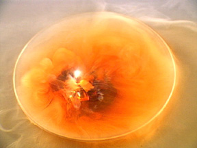 White flames appear atop a red-brown liquid surrounded by yellow-orange dust.