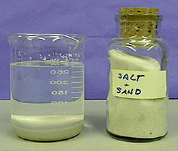 A beaker with an upper layer of cloudy liquid, a white layer of solid, and a yellow layer of solid, and a bottled jar labeled "Salt and Sand"