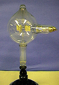 A glass container with electrodes and gold foil paddles on a stand