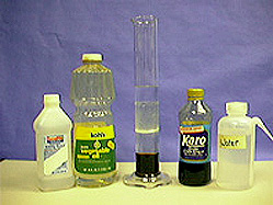 A bottle of alcohol, a bottle of vegetable oil, a glass cylinder with layers of liquids, a suspension, another layer of clear liquid, and a dark liquid. A bottle of Karo syrup and a bottle of water are shown in the photo.