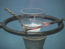A crucible suspended over a burner by wire containing a white solid