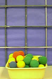 A metal lattice and yellow, green, and orange nerf balls in a yellow tube.