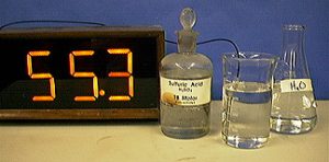 A thermometer, a capped bottle labeled "Sulfuric Acid," a temperature probe with a cable in a beaker and clear liquid, and a flask with clear liquid and label H two O.