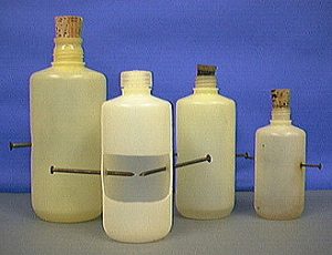 Four capped bottles, three with cork stoppers, with nails protruding from each bottle. One bottle is cut away to reveal the inside.