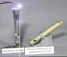A forceps holding a white, glowing solid in a flame over a burner and a corked tube designed for photochemical reactions.