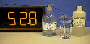 A thermometer, a capped glass bottle labeled "Hydrochloric Acid," a temperature probe with a cable in a clear liquid inside a beaker, and a capped plastic bottle labeled "Sodium Hydroxide"