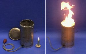 Two photos: In the first photo, an open can with its lid, a red bulb and a tube attached to a can, and a burning candle in a holder. In the second photo, a flame rising from the can with attached tubing.