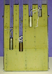 Four metal cylinders with strings each melt yellow beeswax on a plastic tray a different distance.