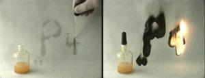 A two photo sequence: A bottle with orange-yellow liquid and hand using an eyedropper with liquid to write the letter "P" and the number four. In the second photo, a capped bottle with orange-yellow liquid and eyedropper, a black char shaped like the letter "P" and an orange flame in the shape of the number four.