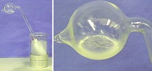 The first photo shows a tube with a bulb-shaped end in a glass Dewar flask with cloudy liquid inside a silver container. The second photo shows clear, cracked solid surrounded by a white halo inside the bulb-shaped end.