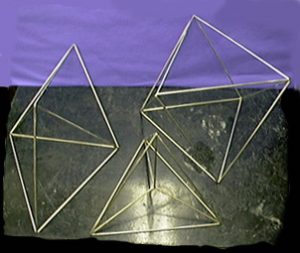 Three geometric shapes made of metal rods on a dark surface.