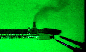 Gas rises in the shadow of a copper-wound tube with hose barb against a green background. An electrode appears in the lower right corner.