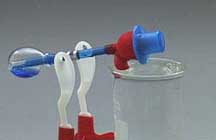A toy bird with a blue top hat and blue liquid in its abdomen dunks its beak into clear liquid inside a beaker.