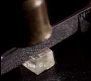 A copper colored object strikes a knife edge that has been placed on a crystal