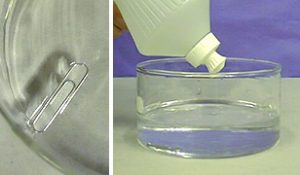 The first photo shows a metal paper clip and its shadow in a glass container with clear liquid. The second photo shows a capped plastic bottle over a clear liquid in a round container. A paper clip rests at the bottom of the lower left side in the container.