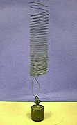 A coiled spring with looped wire attached to a dark weight