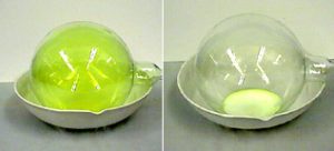 A two-photo sequence: In the first photo, a round flask contains green gas in liquid inside a white bowl. In the second photo, a clear round flask contains pale liquid inside a white bowl.