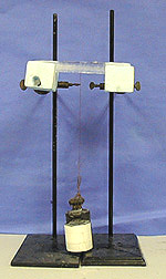 A stick of ice held between two white blocks supported by ring stands. A wire attached to the ice holds two weights with lower white portions beneath the ice.
