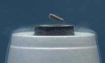 A black magnet floats above a black cylinder-shaped surface and a white base and vapor surrounds surface and base.