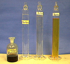 A stoppered, labeled bottle with dark liquid. Three stoppered, labeled glass columns, two with clear liquids and one with brown orange liquid.