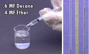 In the first photo, a gloved hand holds a syringe of colorless and clear liquid drawn from the beaker. The amount of decane and ether appear on the photo. The second photo shows a measuring device between two glass tubes with different amounts of silver liquid.