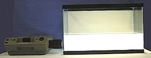 A slide projector points toward an aquarium half-filled with cloudy white liquid against a dark blue background.