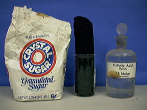 A paper bag labeled granulated sugar, a black solid inside a beaker, and a capped, labeled bottle with clear liquid