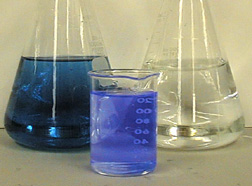 A flask with dark blue liquid, a beaker with cloudy glowing blue liquid, and a flask with clear colorless liquid.
