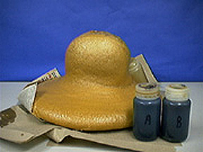 A solid yellow foam and two capped containers with brown liquids top newspaper and paper towels.