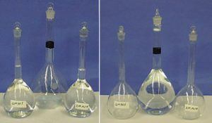 Two photos, each with three stoppered flasks. In the first photo, a labeled flask contains clear liquid, a flask with a black band is empty, and a second labeled flask contains clear liquid. In the second photo, the flask with the black band contains liquid that reaches above the black band and a layer of blue liquid appears at the bottom of the flask. The remaining two flasks are empty.