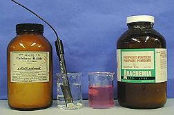 A capped, labeled bottle, a probe with attached cable in clear liquid and solid in a beaker, a beaker with pink liquid, and a capped, labeled amber bottle