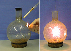In the first photo, a cigarette holder and a lit cigarette appears next to a stoppered flask with black flecks on a cork ring. A hand holds a burning match next to the flask. In the second photo, white light surrounded by orange sparks illuminates the flask.