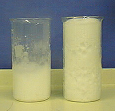 Two beakers; the beaker on the left is half-filled with white solid and foam. The beaker on the right is filled with white solid and copious foam.