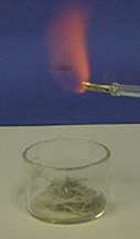 Orange flame from a glass tube over a mass of gray solid in a container