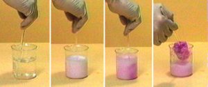 A four-photo sequence: A hand uses a stir rod to stir a clear liquid in a beaker. In the second photo, a hand uses a stir rod in the liquid with a white upper layer in the liquid in the beaker. In the third photo, the mixture is pink with dark pink layers on the right side of the beaker. In the fourth photo, a hand uses the stir rod to lift a red-pink solid from the pink mixture in the beaker.