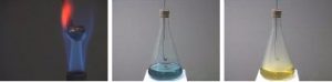 A black spoon in a blue and orange frame. A flask with a spoon and cork stopper assembly with a blue liquid. A flask with a spoon and a cork stopper assembly with a yellow liquid.