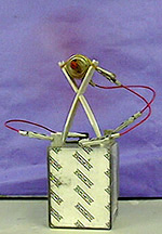 A specialized electrochemical cell is connected by wires to a small electrical motor. A red propellor spins.