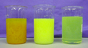 A beaker with an upper layer of yellow liquid and red-orange solids, a beaker with yellow-green solid, and a beaker with cloudy yellow liquid