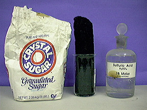 A paper bag labeled granulated sugar, a black solid inside a beaker, and a capped, labeled bottle with clear liquid