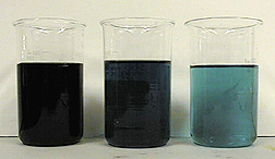 Three beakers, two containing dark liquids and one containing a light blue liquid