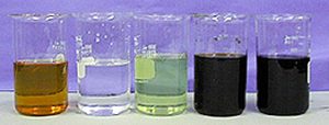 A beaker with clear orange liquid, a beaker with clear colorless liquid, a beaker with clear light green liquid, and two beakers with dark red and blue liquids