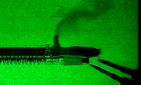 Gas rises in the shadow of a copper-wound tube with hose barb against a green background. An electrode appears in the lower right corner.