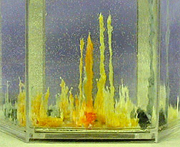 Yellow, white, orange, and dark crystals appear inside a glass tank.