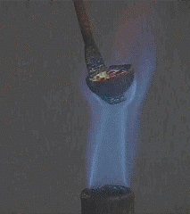A heated spoon is placed in a flask with blue liquid. The liquid changes from blue to green to yellow. Vapor coats the glass.