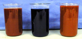 Three beakers, two with red liquids and one with a dark colored liquid