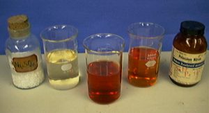 A pale red solution in one beaker and a fading of color in a second beaker indicate a chemical reaction.