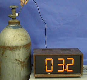 A hand holds a temperature probe next to the opening of a gas tank, and the thermometer displays a readout.