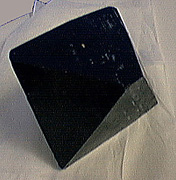 A black octahedral crystal showing five vertices resting on paper.