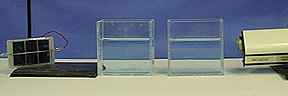 The photo shows a solar cell with wire on a ring stand, two plexiglass tanks with blue water, and a laser. 