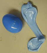 A blue egg-shaped solid next to a light blue solid that has been elongated on a gray surface.